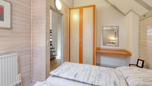 A bedroom with wooden panel walls, a bed with floral bedding, a wooden wardrobe, a bedside table, and a mirror on the wall.