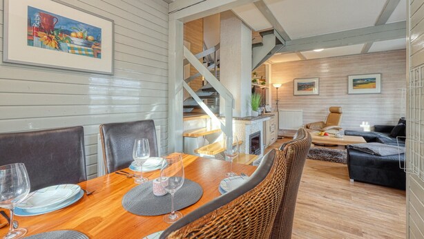 A dining area with a wooden table, chairs, and a staircase leading to a loft.