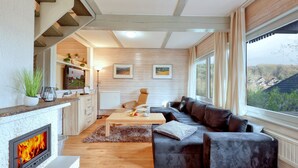A modern living room with a fireplace, a sofa, a TV, and a view of the countryside.