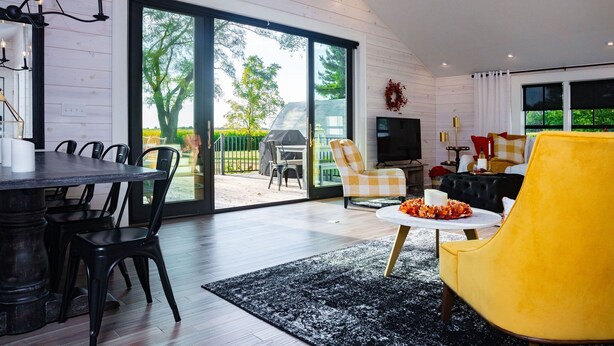 A modern living room with a dining area, large sliding glass doors to a backyard, and a yellow armchair. - Mabel and Harry's, a modern country guest house (Kokomo)