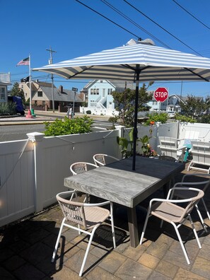 An outdoor patio with a wooden table and wicker chairs, a striped umbrella, and a stop sign in the background. - Beach Block! Beach Tags, Central AC, Grill and Patio! (Seaside Park)