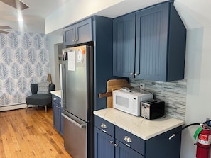 A modern kitchen with dark blue cabinets, a stainless steel refrigerator, a microwave, and a toaster.