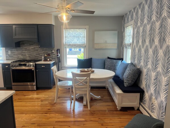 A modern kitchen with a dining area, featuring a round table, white chairs, and a built-in oven. - Beach Block! Beach Tags, Central AC, Grill and Patio! (Seaside Park)