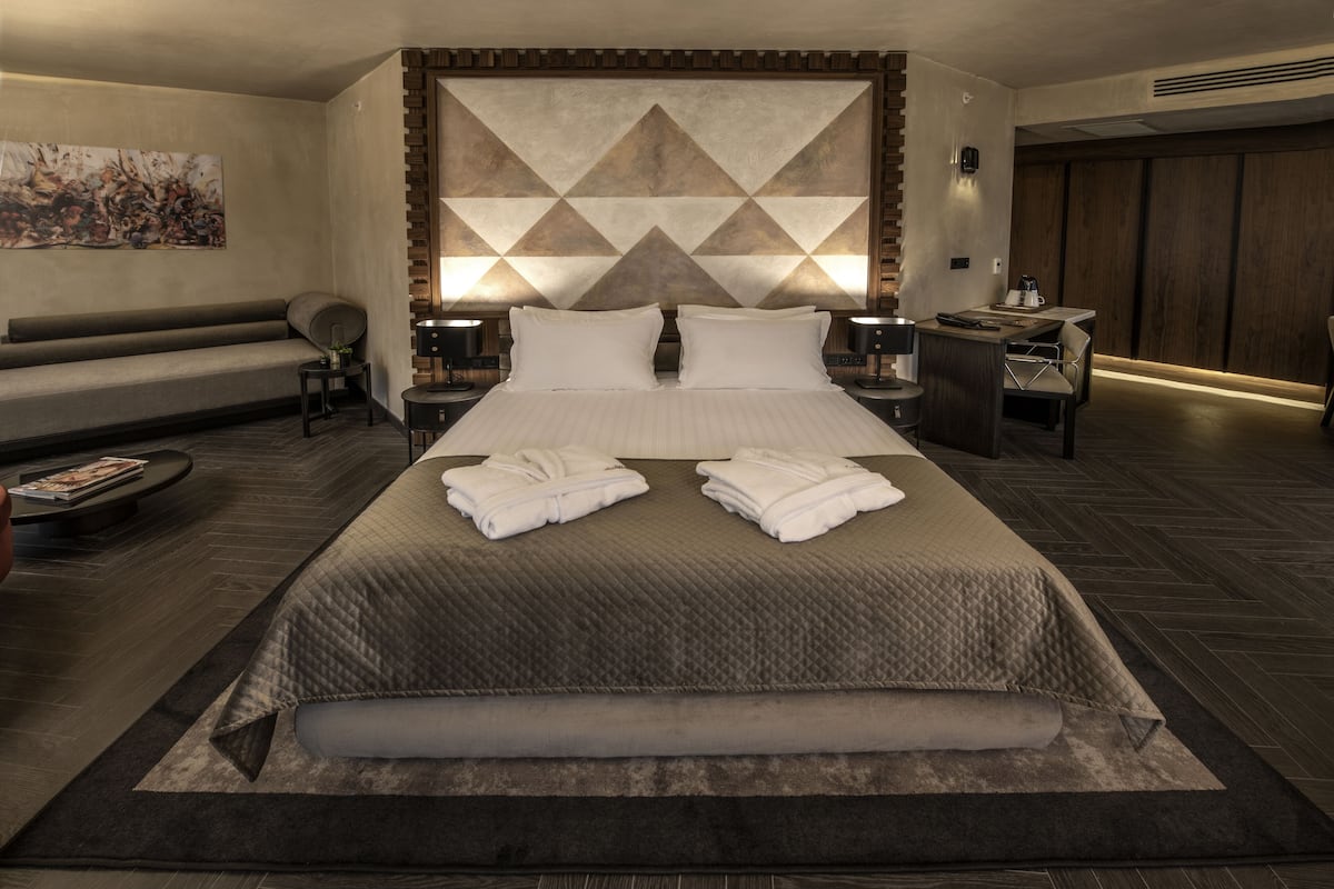 Una habitación de hotel moderna con una cama grande, un sofá, una mesa de centro y un cuadro en la pared.