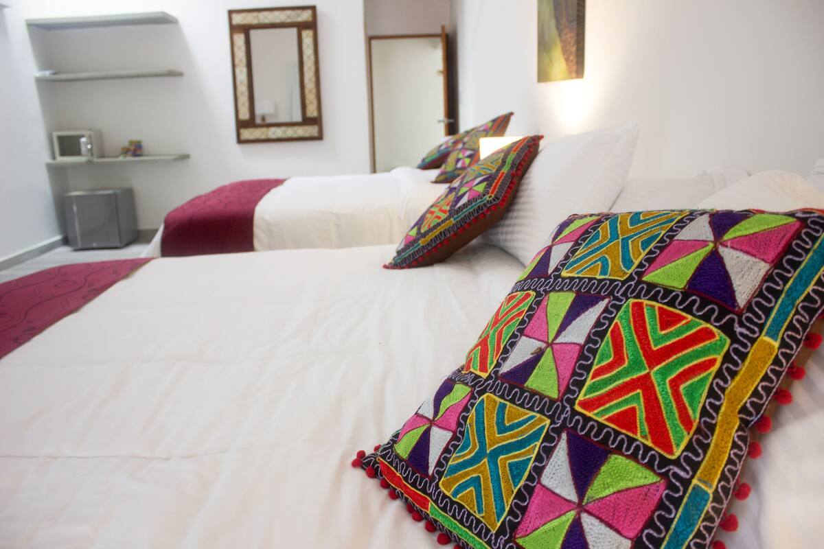 Quarto de hotel com cama bem arrumada, uma mesinha de cabeceira, micro-ondas e guarda-roupa.