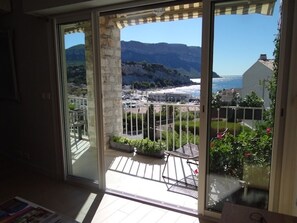 A balcony with a view of a coastal town, a stone pillar, and a metal railing.