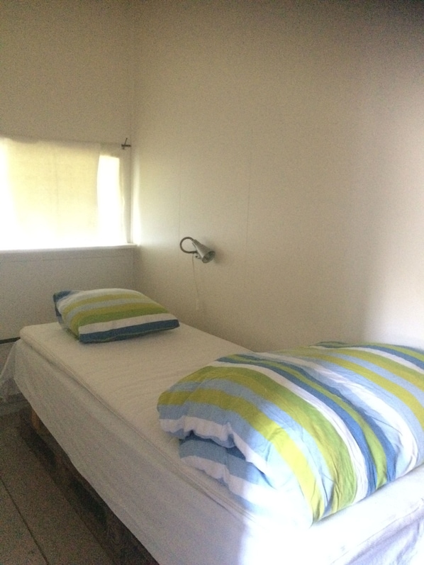 A single bed with a striped pillow and a plain wall.