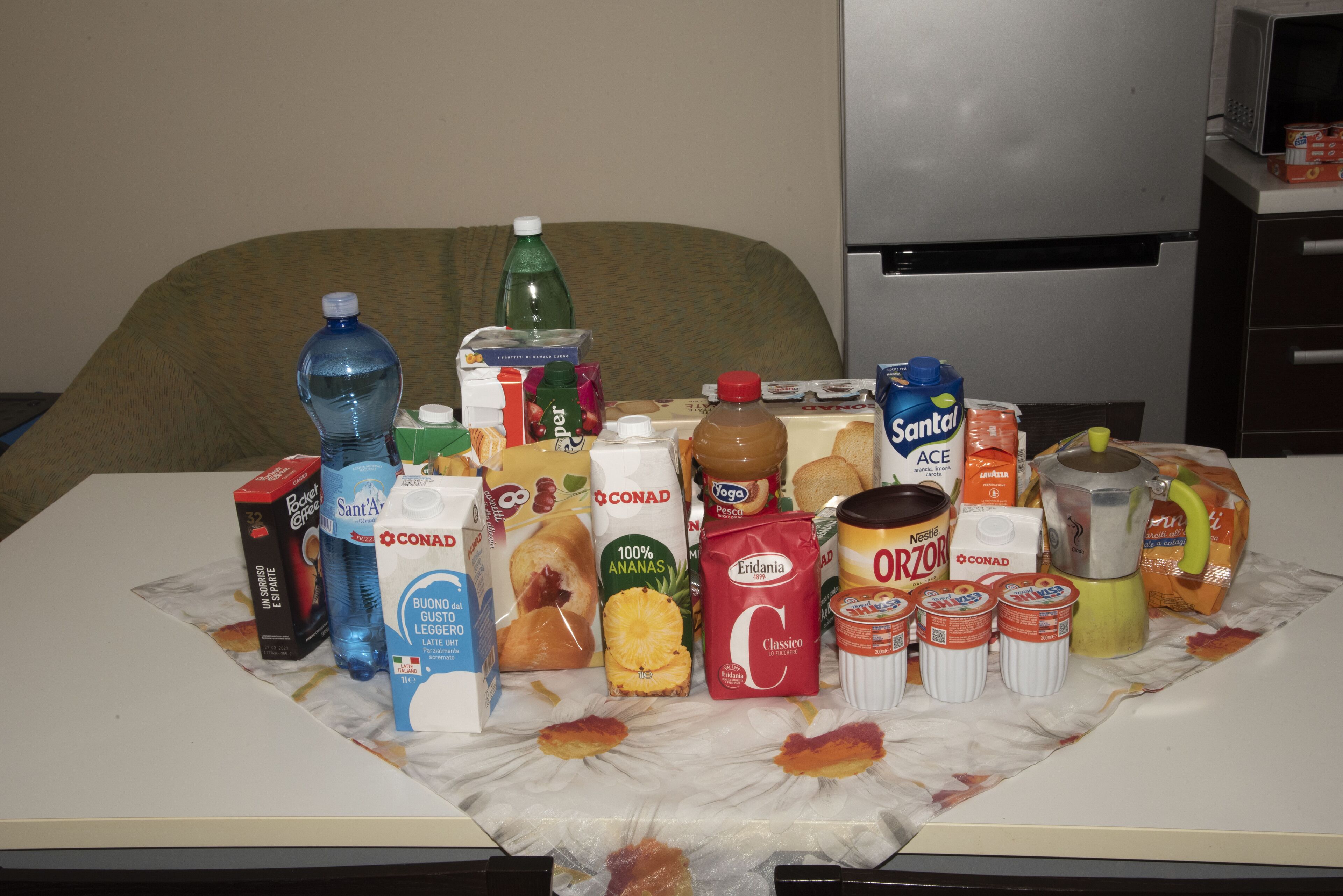 Une table sur laquelle se trouvent divers aliments et boissons, notamment une bouteille d’eau, du jus de fruits et un carton de lait.