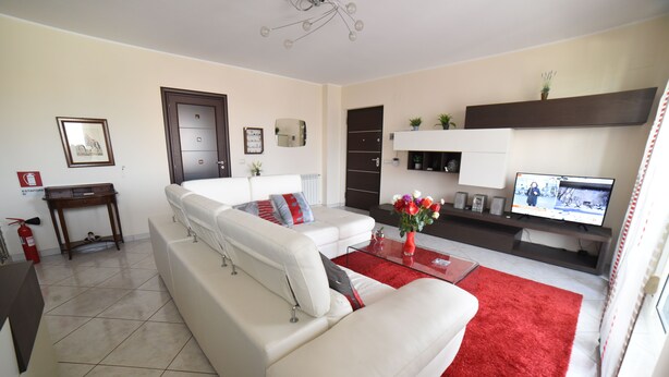A modern living room with a white sofa, red rug, and a television on a stand. - MODERN AND COZY APARTMENT NEAR THE SEA OF RECANATI (Giardini Naxos)