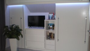 Una habitación con un televisor en un estante, una planta en maceta y un armario blanco.