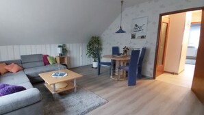 Una sala de estar moderna con un sofá gris, una pequeña mesa de centro de madera, una mesa de comedor con sillas y un ventanal grande.