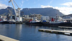A harbor with boats docked, a crane, and buildings in the background. - Rosedene Lodge (Cape Town)