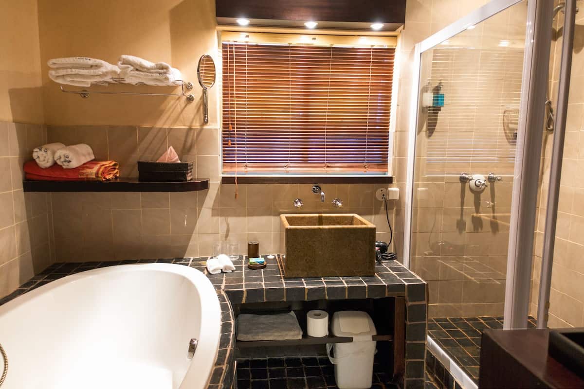 A bathroom with a bathtub, a sink, a shower, and a window with blinds.