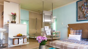 A modern hotel room with a glass coffee table, a bed with plaid bedding, a small bedside table with a lamp, a wall-mounted TV, and a bathroom with a shower and toilet. - Rosedene Lodge (Cape Town)