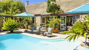 A pool area with lounge chairs and umbrellas, surrounded by potted plants and a stone wall. - Rosedene Lodge (Cape Town)