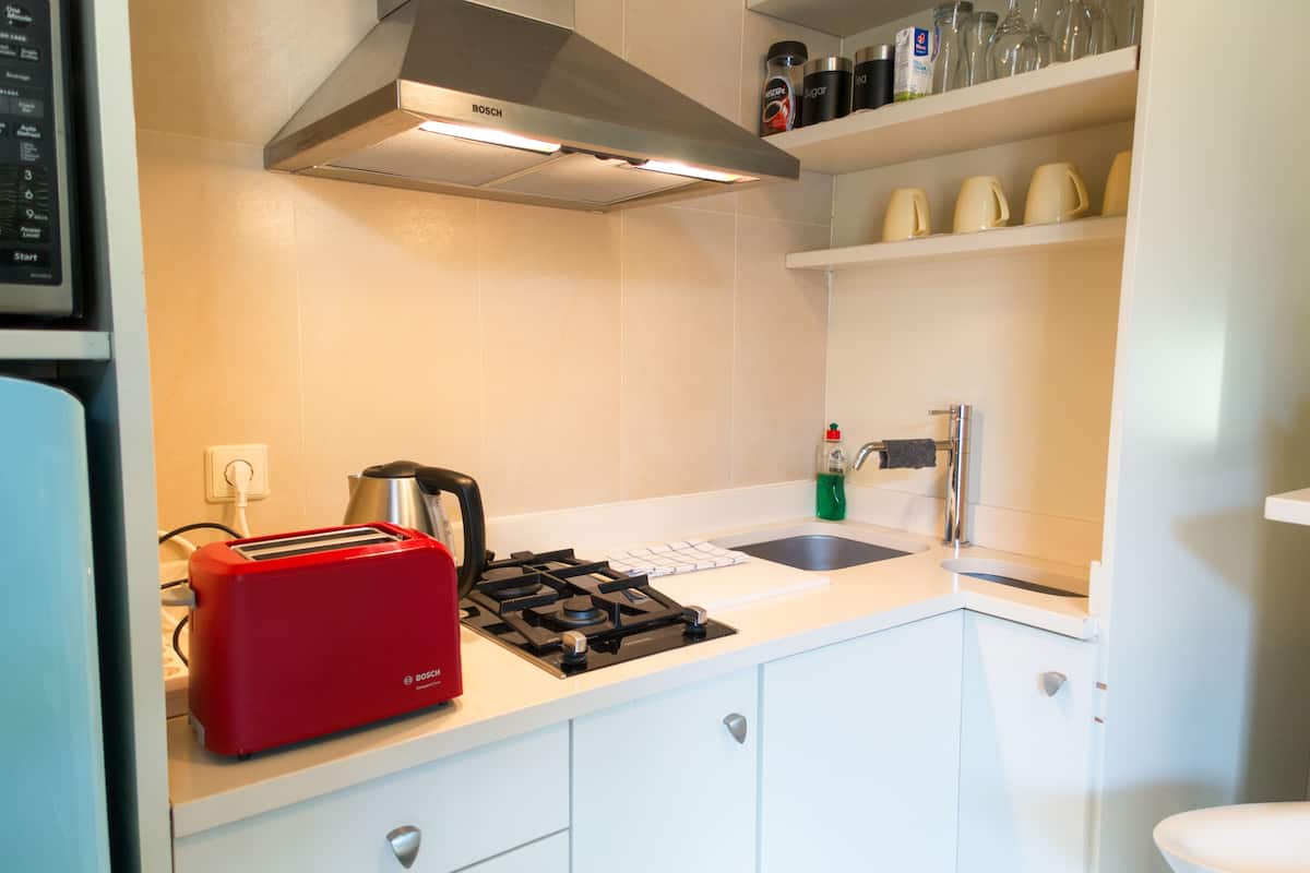 A modern kitchen with white cabinets, a Bosch range hood, a red toaster, and a sink.