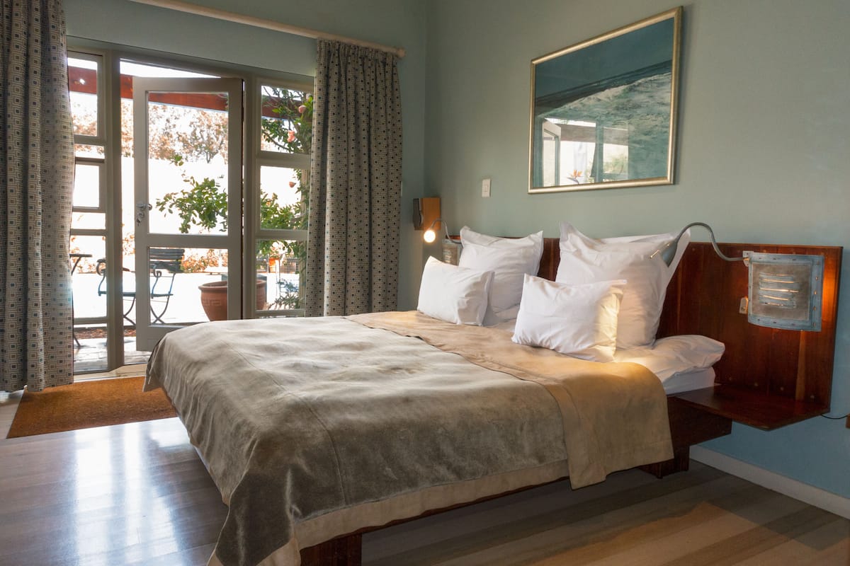 A bedroom with a bed, a nightstand, a window with curtains, and a view of the outdoors.