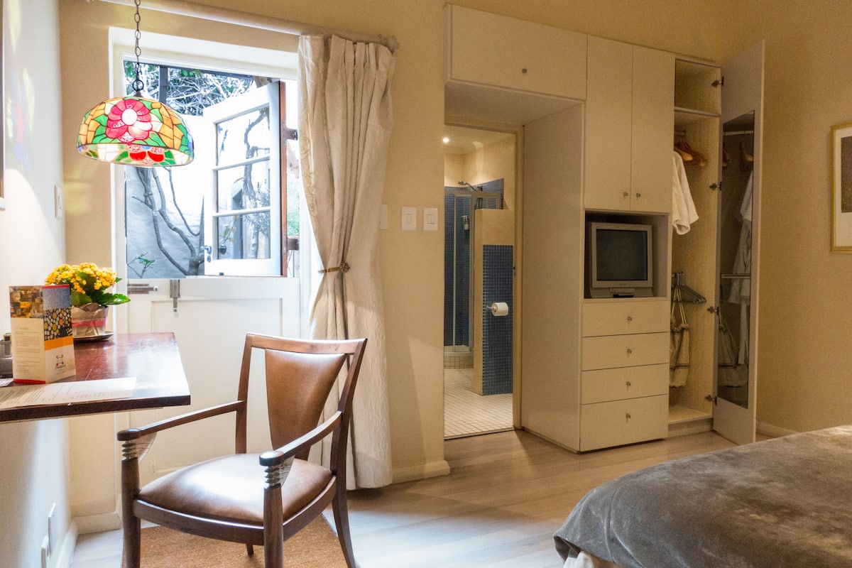A bedroom with a bed, a desk with a chair, a TV, and a bathroom with a shower and a toilet.