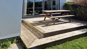 Ein zweistöckiges Haus mit einer großen Glasgalerie, einer Holzterrasse und einem Picknicktisch.