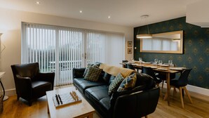 Ein modernes Wohnzimmer mit einem schwarzen Ledersofa, einem Couchtisch aus Holz und einem Essbereich mit einem Holztisch und Stühlen.