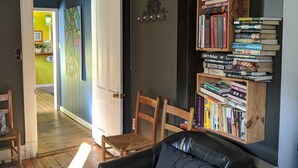 Uma sala de estar acolhedora com um sofá de couro preto, cadeiras de madeira, uma estante cheia de livros e teto de madeira.
