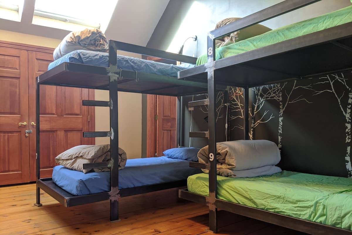A dormitory room with bunk beds, wooden floors, and a large window.