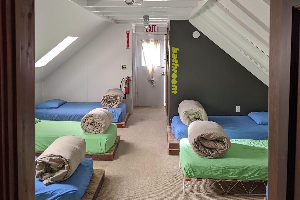 A dormitory room with four beds, a visible exit sign, and a bathroom sign.