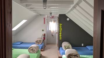 A dormitory room with four beds, a visible exit sign, and a bathroom sign.