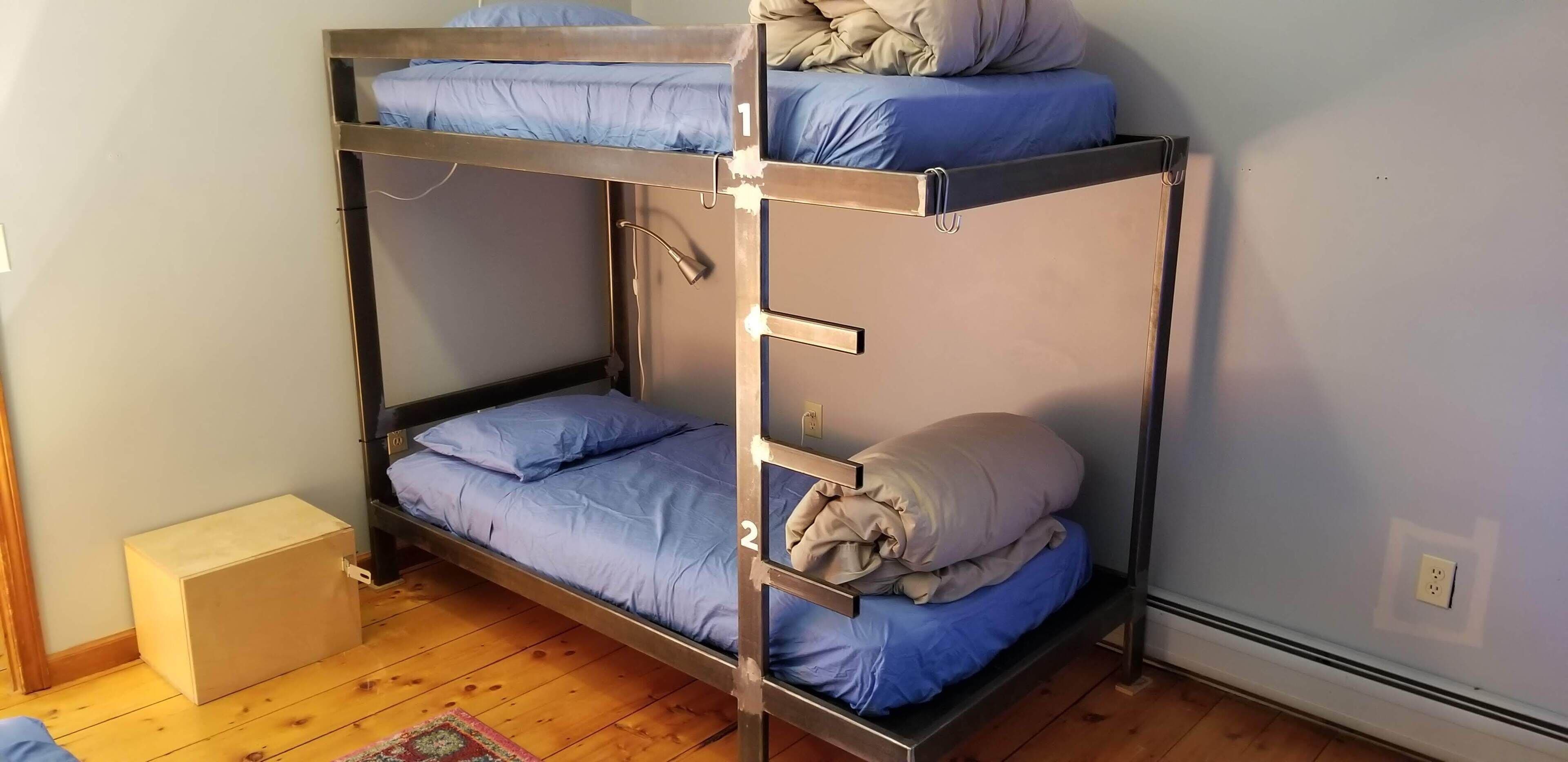 Una cama litera con dos niveles, un pequeño cofre de madera y un calentador en el suelo.