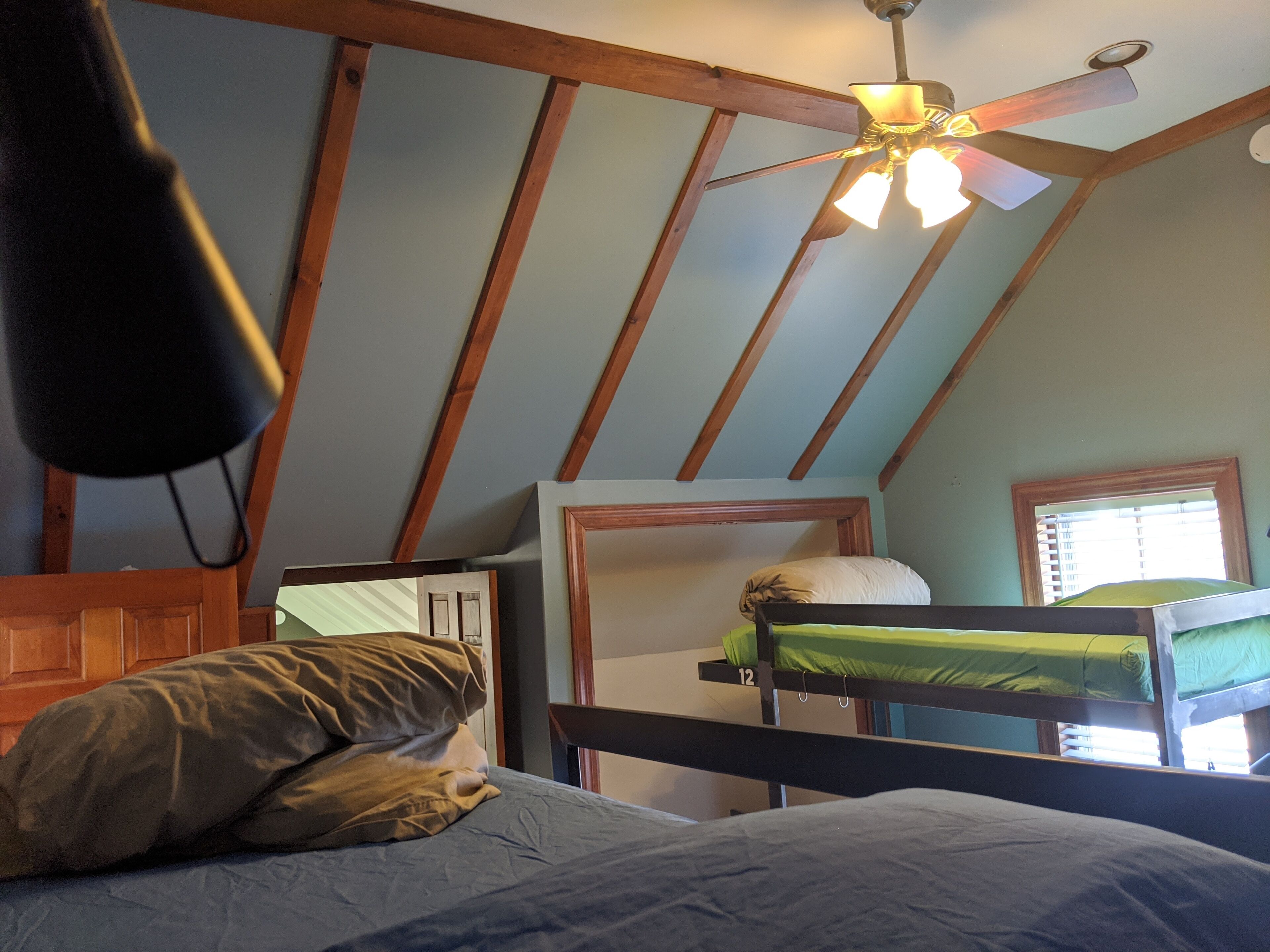 A dormitory room with bunk beds, a ceiling fan, and a window with blinds.