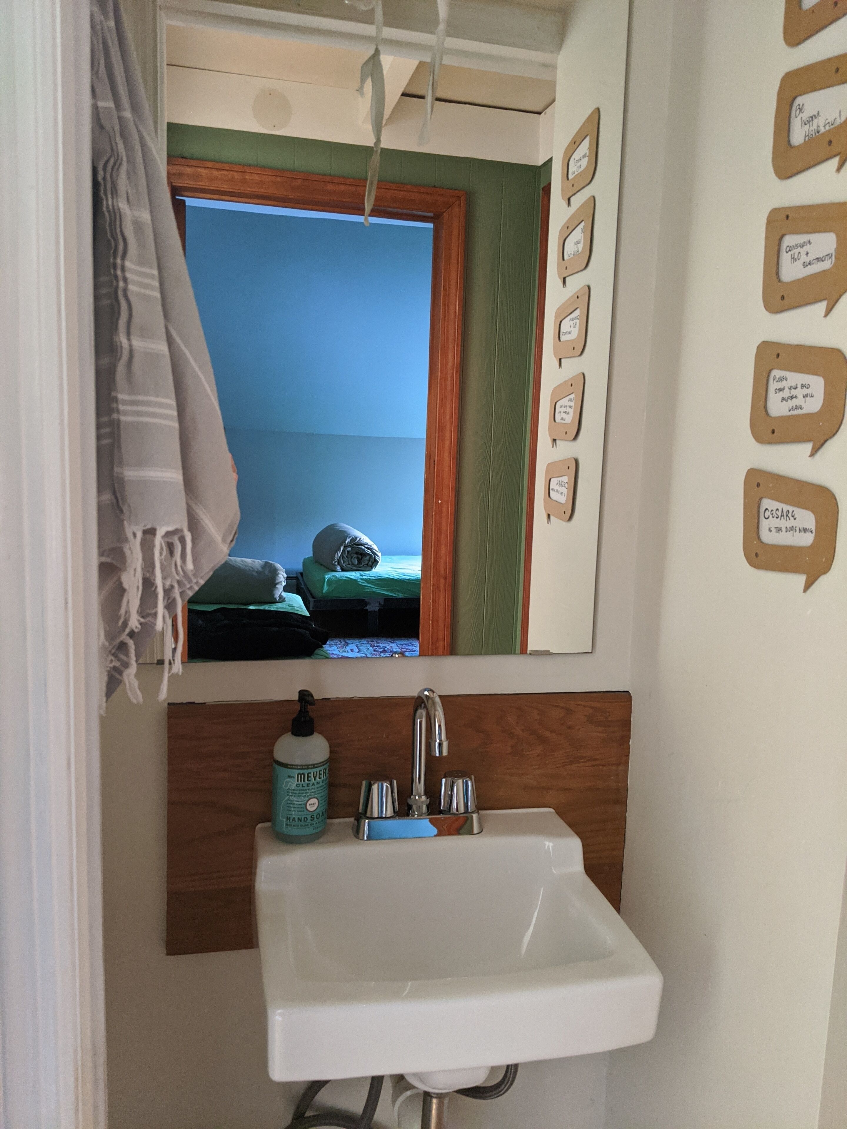 Une salle de bain avec un lavabo, un miroir et une fenêtre donnant sur la mer. Des bulles de dialogue contenant des citations motivantes sont peintes sur le mur.