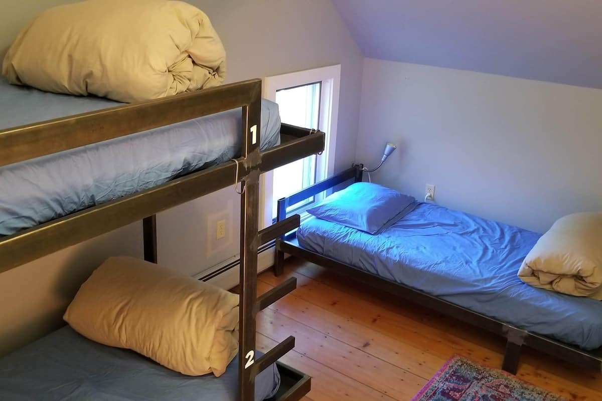 A dormitory-style room with bunk beds, a window, and a fan.