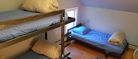 A dormitory-style room with bunk beds, a window, and a fan.