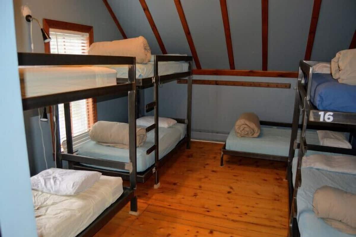 A dormitory room with bunk beds, wooden floors, and a window with blinds.