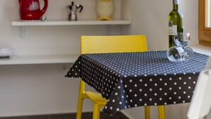 Un coin repas avec une table recouverte d’une nappe à pois, une chaise jaune et une bouteille de vin posée sur la table.