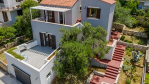 Une maison moderne à deux étages, dotée d’un toit plat, d’un patio couvert et d’un chemin en pierre menant à l’entrée.