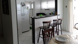 A kitchen with a central island, two wooden chairs, and a dining table with a plate and a bowl. - Florida Beach Resort (Praia Grande) - Sea Front (praia grande)