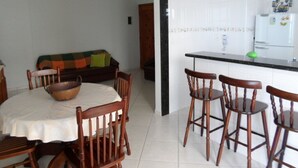 A dining area with a round table and wooden chairs, a kitchen with a refrigerator and a microwave, and a sofa in the background. - Florida Beach Resort (Praia Grande) - Sea Front (praia grande)