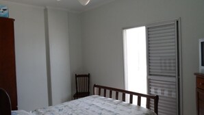 A bedroom with a bed, a chair, a ceiling fan, a window with blinds, and a wooden dresser. - Florida Beach Resort (Praia Grande) - Sea Front (praia grande)