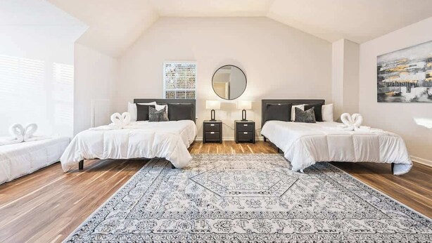 Un dormitorio con dos camas, un tapete grande, un espejo y un cuadro en la pared.