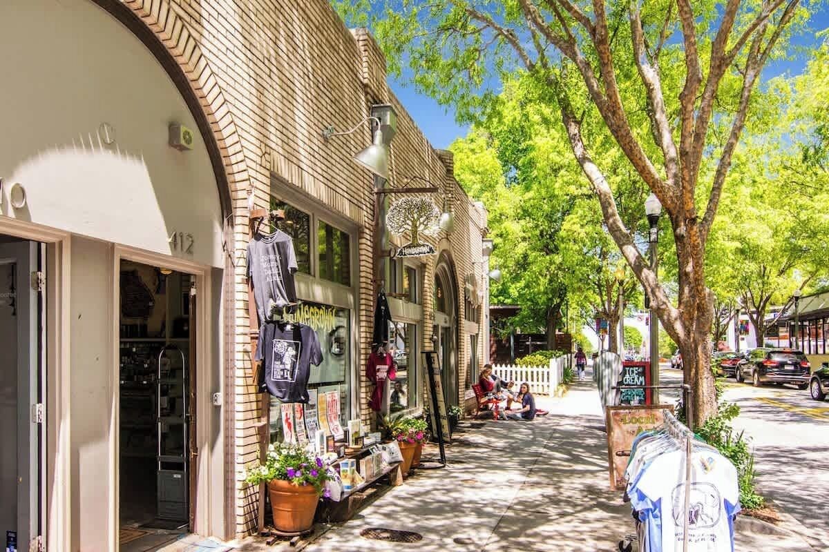 A street with shops, outdoor seating, and a tree-lined sidewalk.