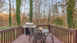 Una terraza de madera con una parrilla, sillas y una mesa.