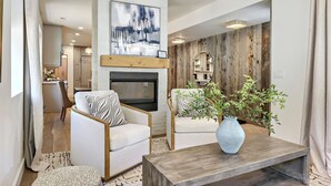 A modern living room with a fireplace, two white armchairs, a coffee table, and a large abstract painting.