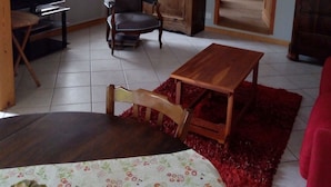 A living room with a wooden cabinet, a television, a chair, and a red rug. - House, large balcony with stairs down to the garden. (L'Argentière-la-Bessée)