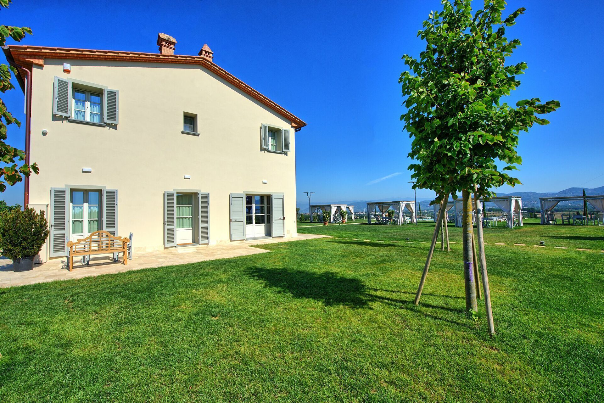 A two-story house with a well-maintained lawn, a bench, and a tree.