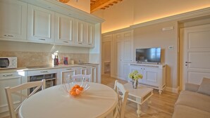 Une cuisine moderne avec des meubles blancs, un coin repas doté d’une table ronde et un salon avec un canapé et un téléviseur.