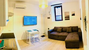 Ein modernes Wohnzimmer mit einer Eckcouch, einem Flachbildfernseher, einem kleinen Tisch und einer Heizung.