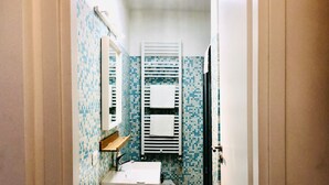 Ein schmales Badezimmer mit einem weißen Waschbecken, einem Spiegel und einer Toilette. Die Wände sind mit blau-weißen Mustern gefliest.