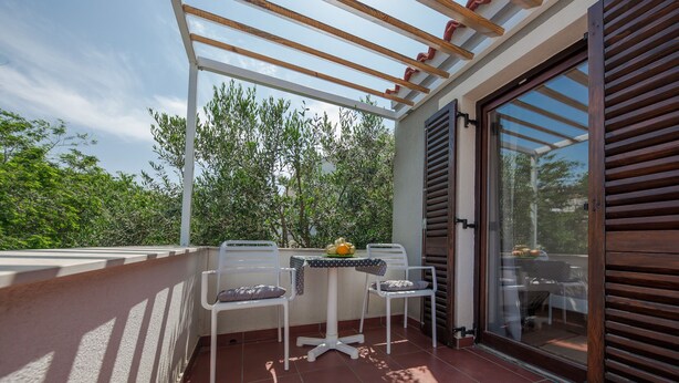 A balcony with a table and two chairs, a wooden pergola, and a sliding glass door.