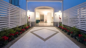 A hotel entrance with a geometric tiled floor, white slatted fences, and red flamingo statues. - Jacaranda House - My Rental Homes (Sant'Agnello)